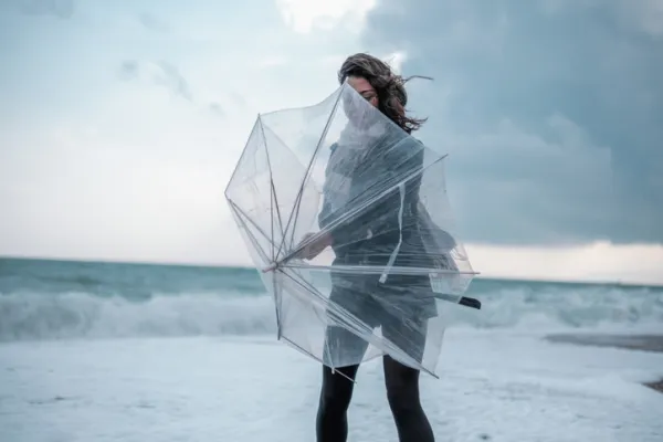 Sad young woman walking alone on the beach with umbrella in rainy weather