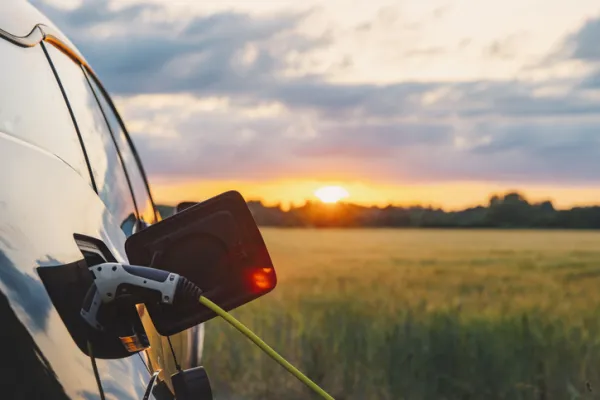An electric car plugged in against a background of a rural location at sunset