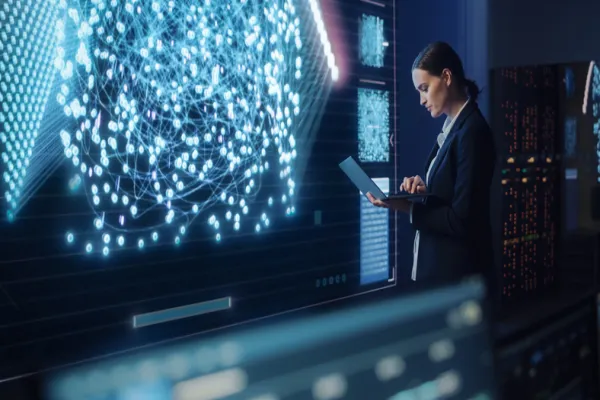 Young Female Computer Science Engineer Working on Laptop next at Big Screen Display Showing Neural Data. Telecommunications Technology Company System Control and Monitoring Room with Servers.