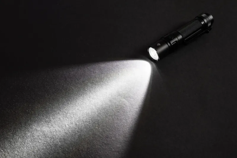 Flashlight and a beam of light in darkness. A modern led lamp with bright projection on dark wood table.