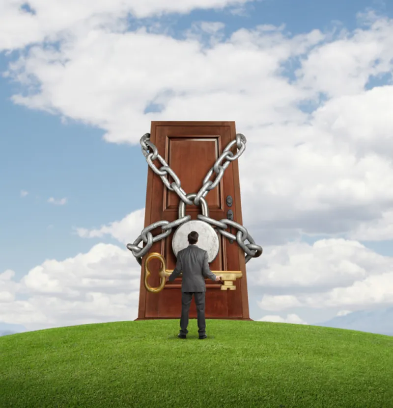 Businessman holding large key looking up at padlocked door